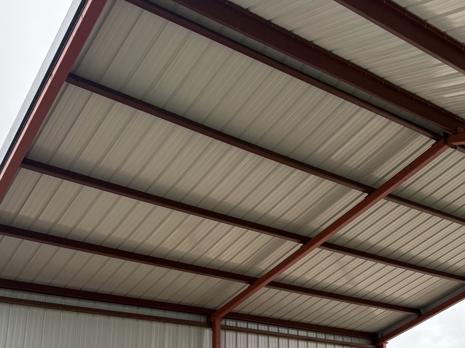 Looking up under a pole barn roof at metal panels on red framing, with open sides
