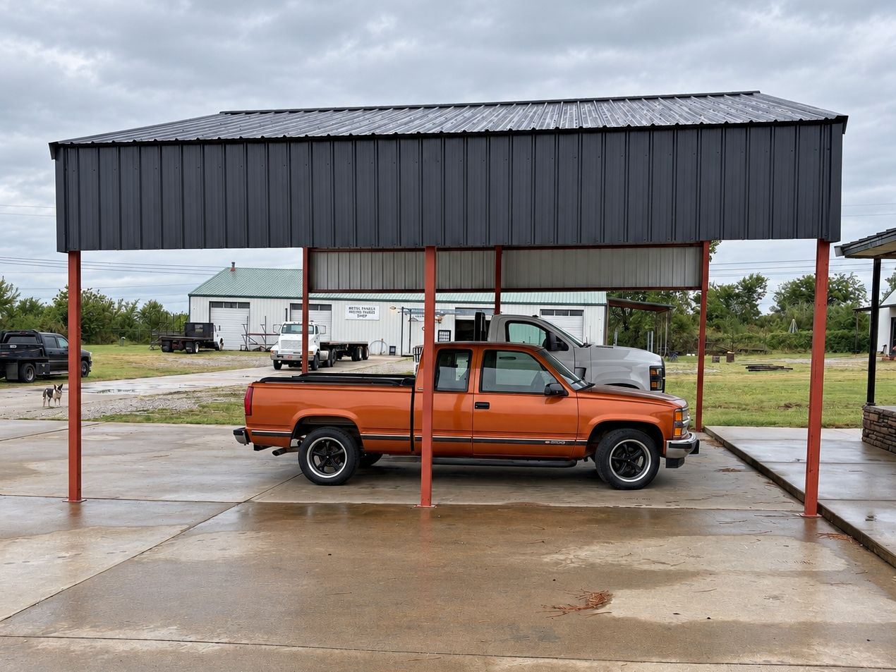 Side view of an open pole barn with a charcoal upper wall and an orange pickup parked under it