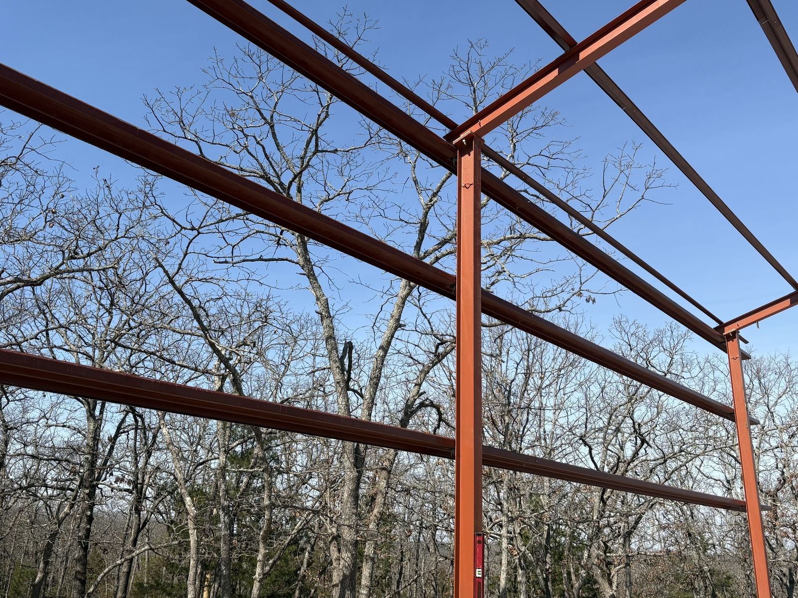 Red steel building frame standing on a new concrete slab among trees