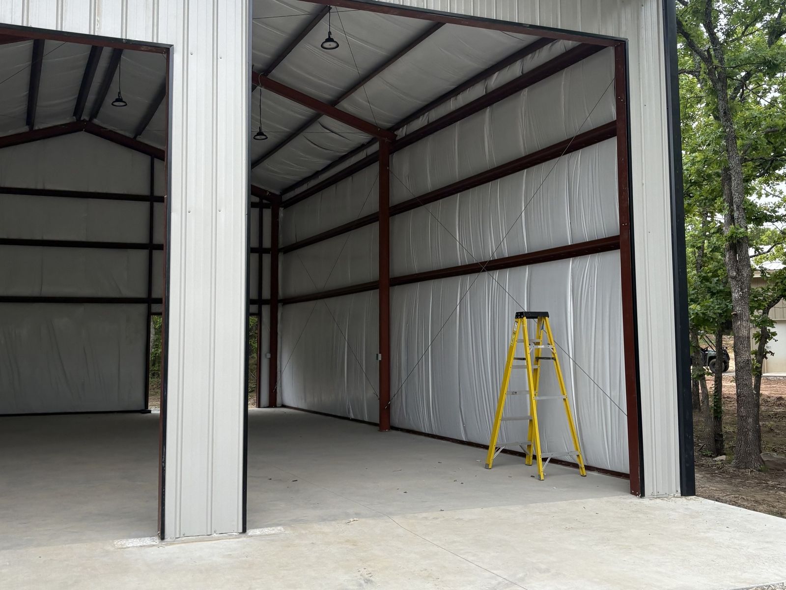 Tall open door into an insulated steel building with red framing and a concrete floor