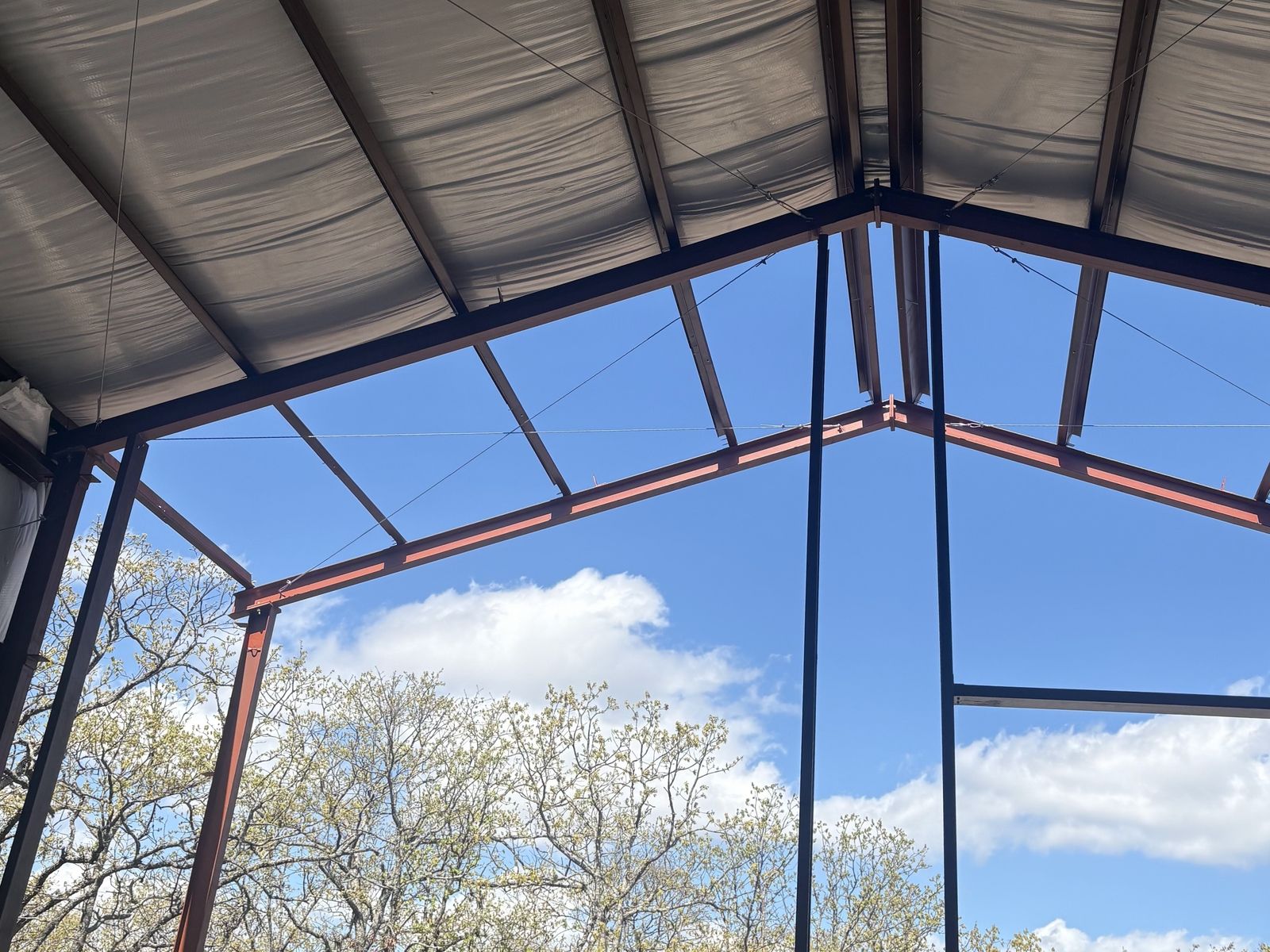 Metal building roof on red steel framing with open walls and blue sky