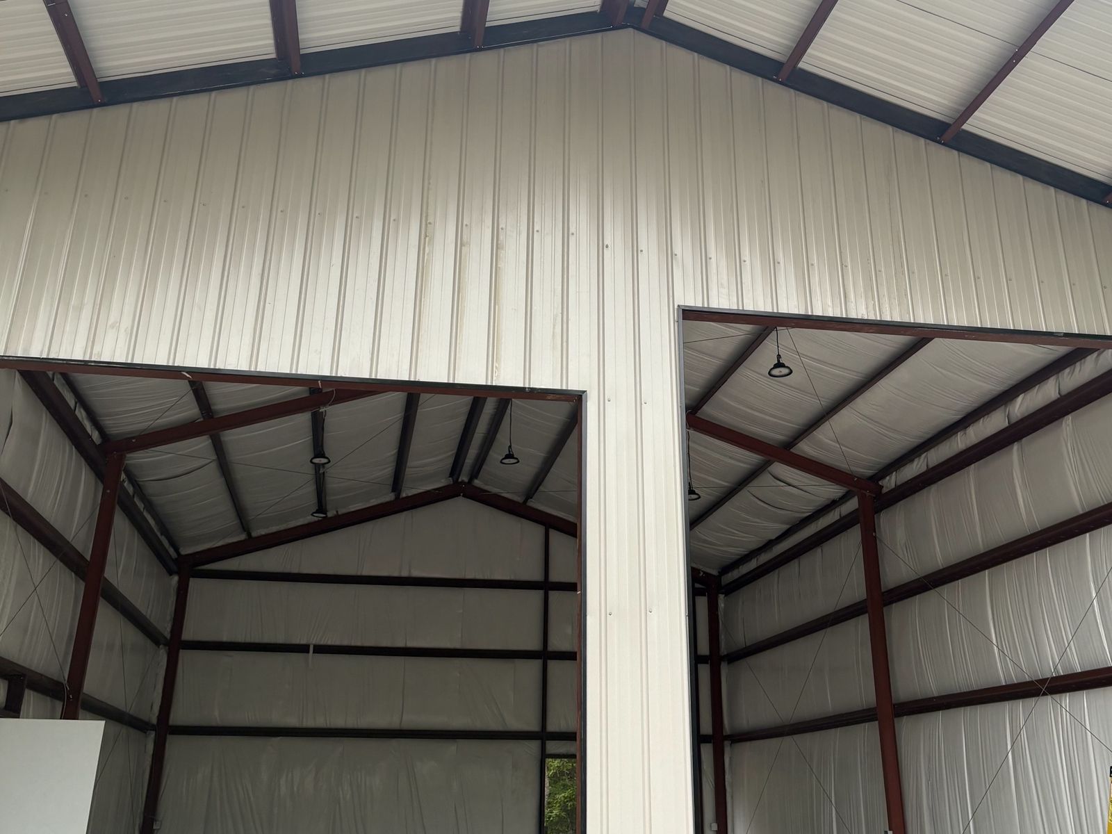 White metal building with two open bays and red steel framing inside