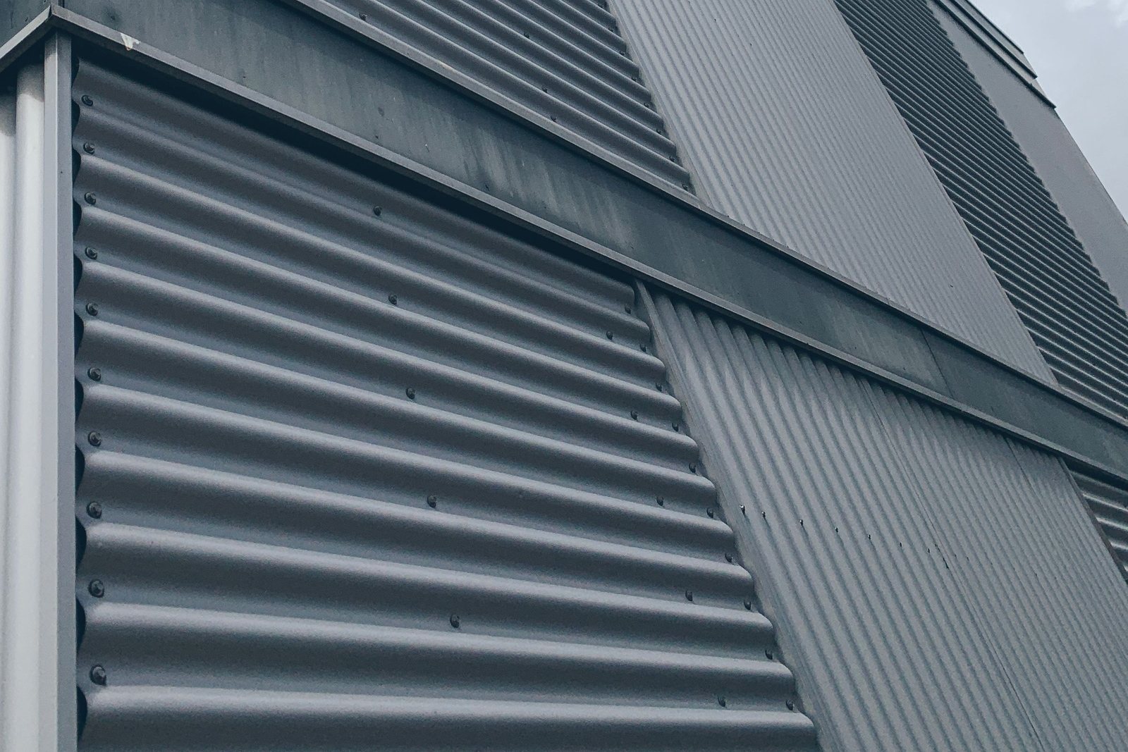 Corrugated metal wall cladding wrapping the corner of a building against a gray sky