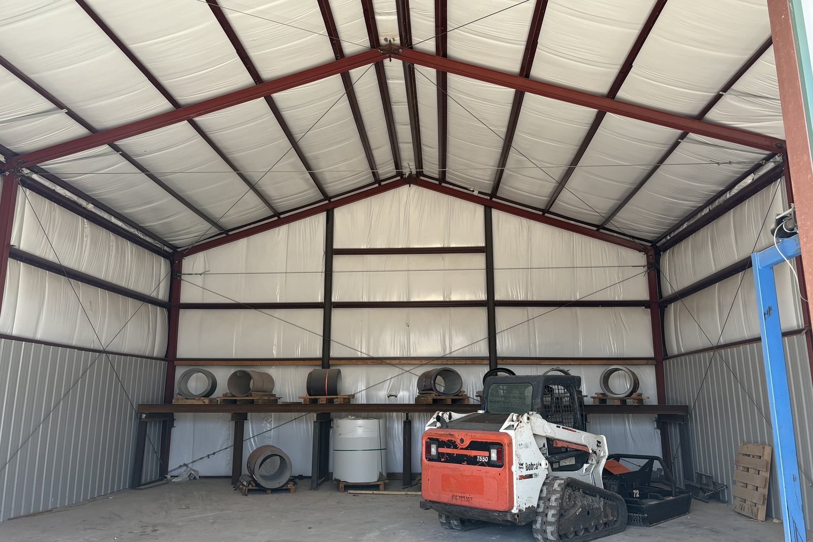 Skid steer and stored metal coils inside an insulated steel building