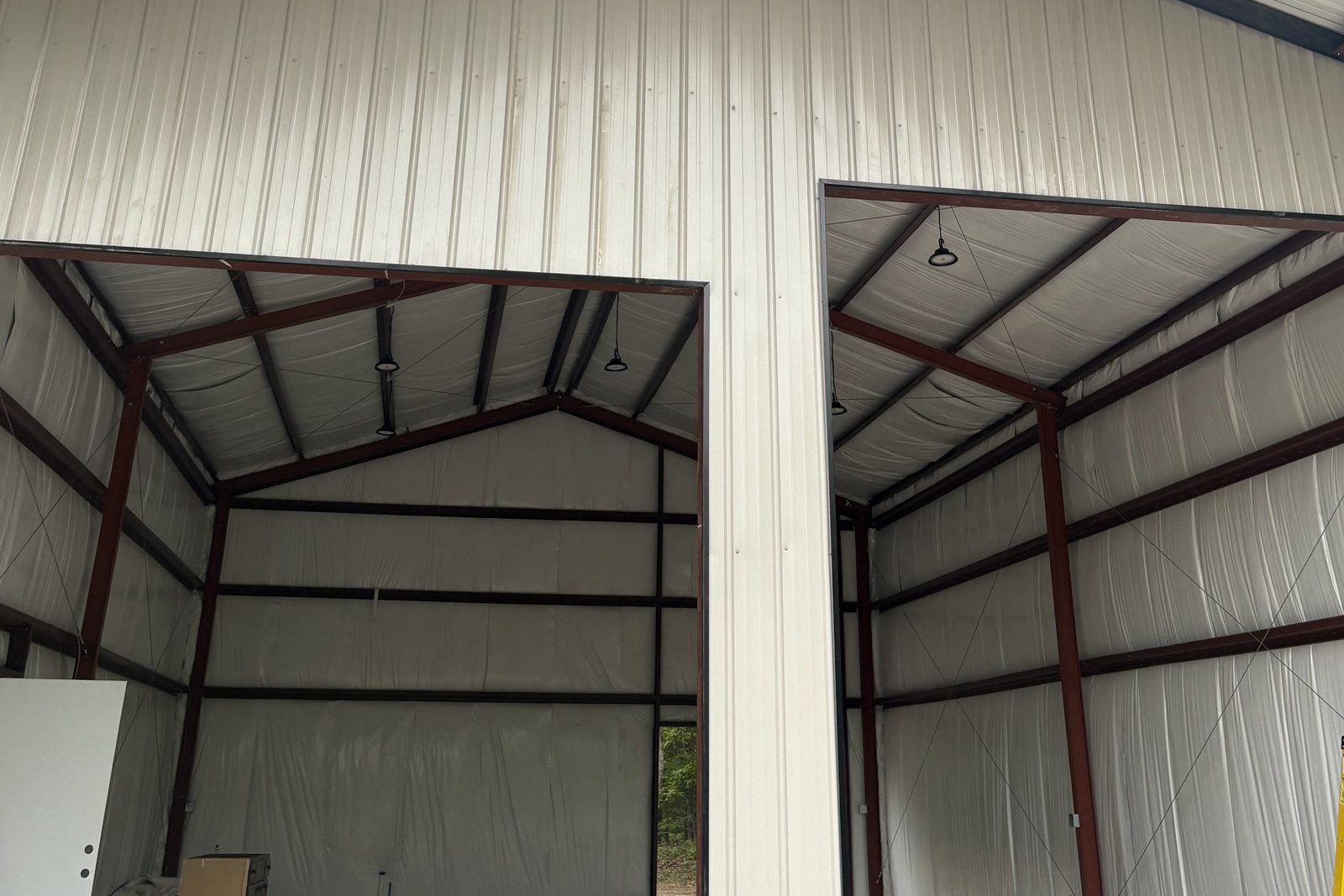 Two open bays inside a white steel building with red framing and a ladder
